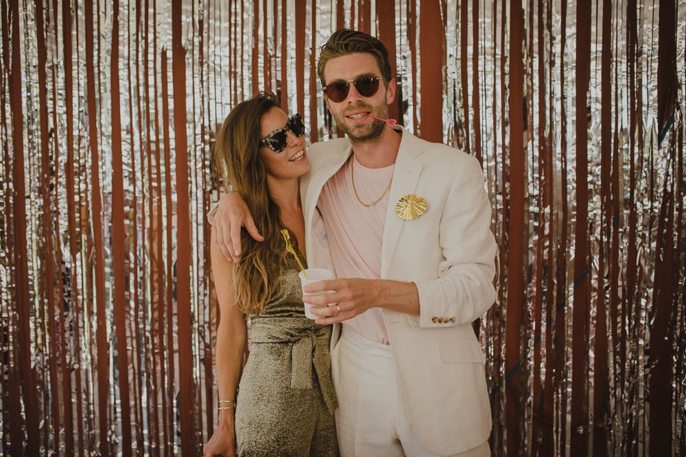 Stylish couple in summer attire pose against metallic corrugated wall backdrop.