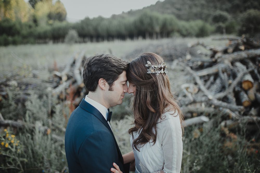 A romantic couple shares an intimate moment outdoors against a rustic backdrop of stacked wood.