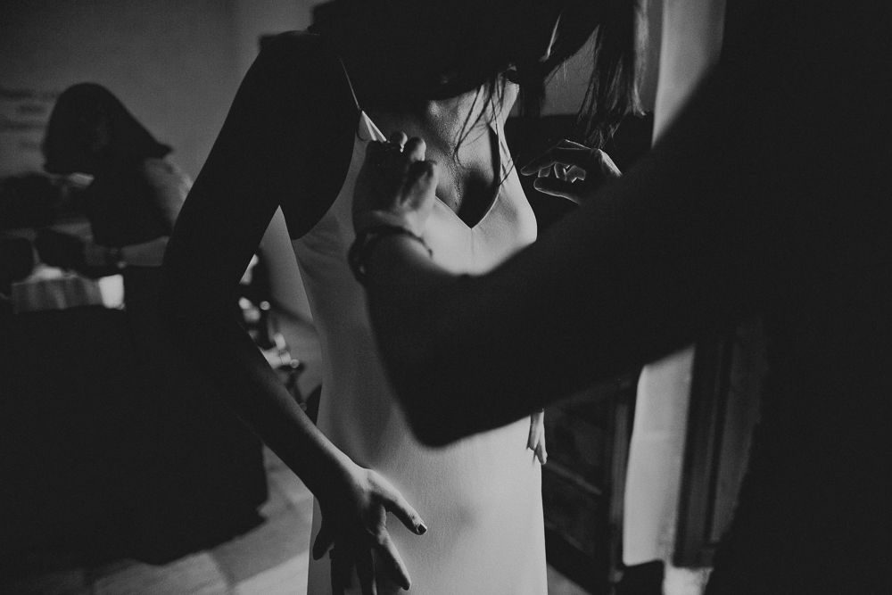 Black and white image of someone adjusting clothing details in dim lighting.