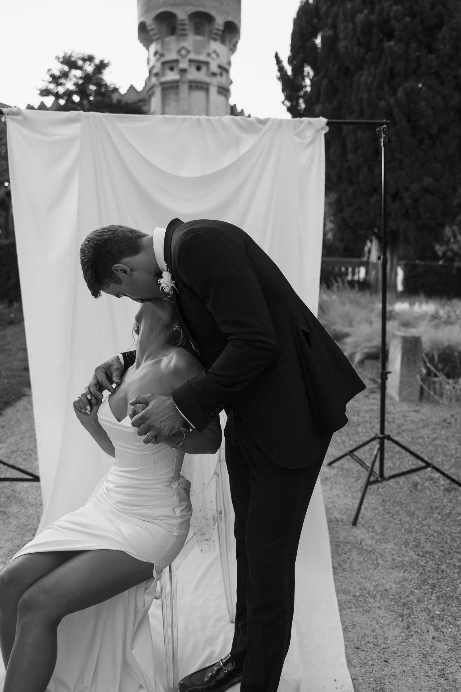 Intimate black and white portrait of couple against white backdrop with castle tower visible.