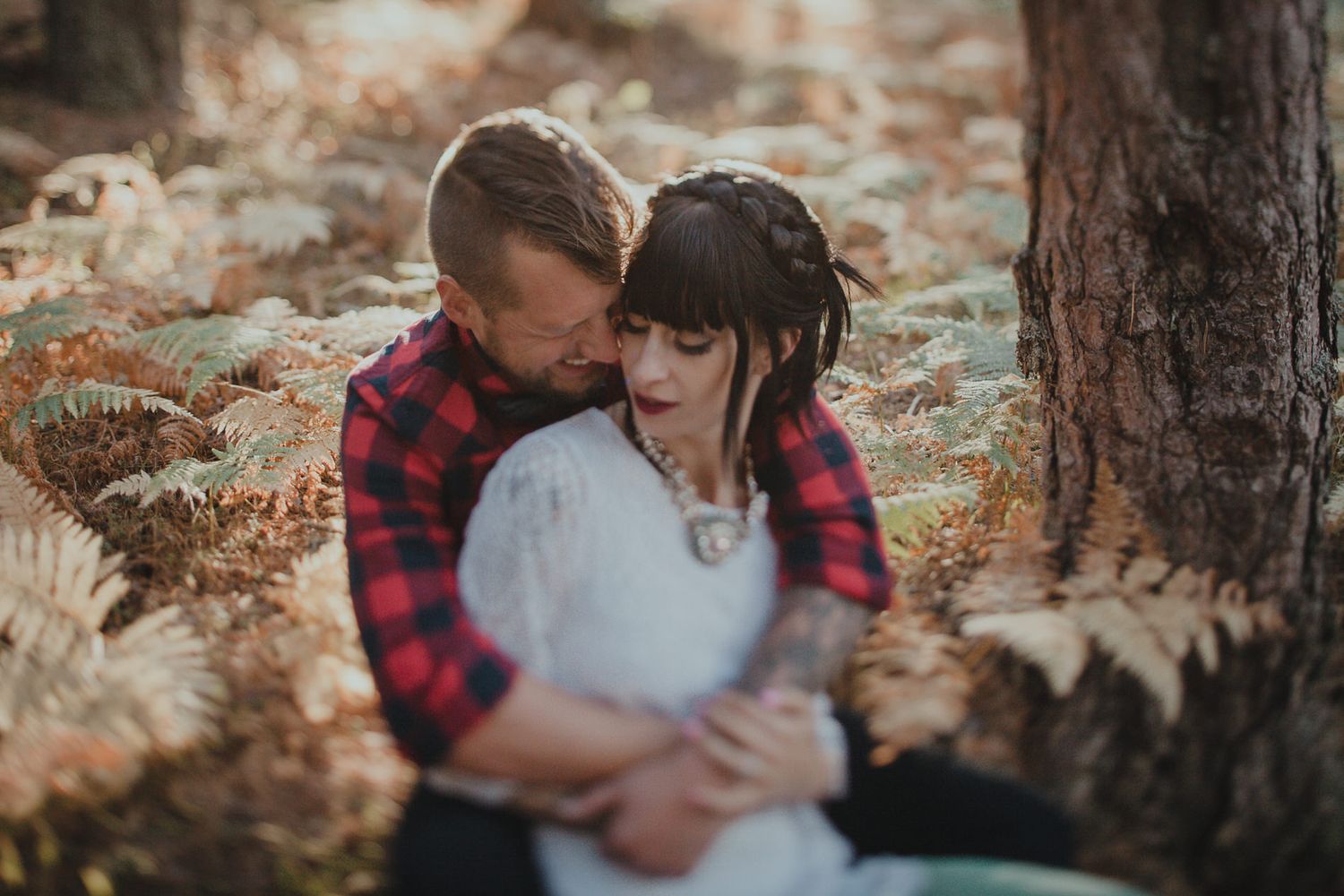 Intimate forest portrait with couple in plaid shirt and white dress among autumn ferns.