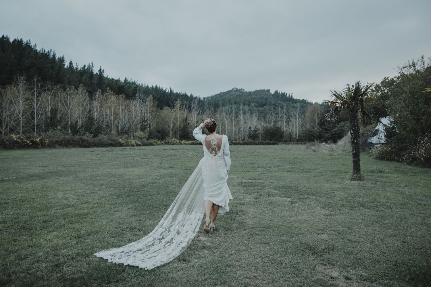 A bride in a flowing white dress twirls in a misty field with mountains in the background.