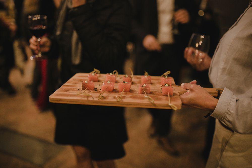 Server holding wooden board with appetizers at evening event.