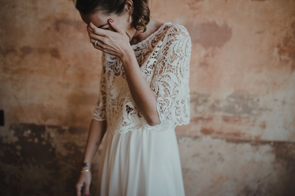 An elegant bridal gown featuring a delicate lace top and flowing white skirt photographed against textured walls.