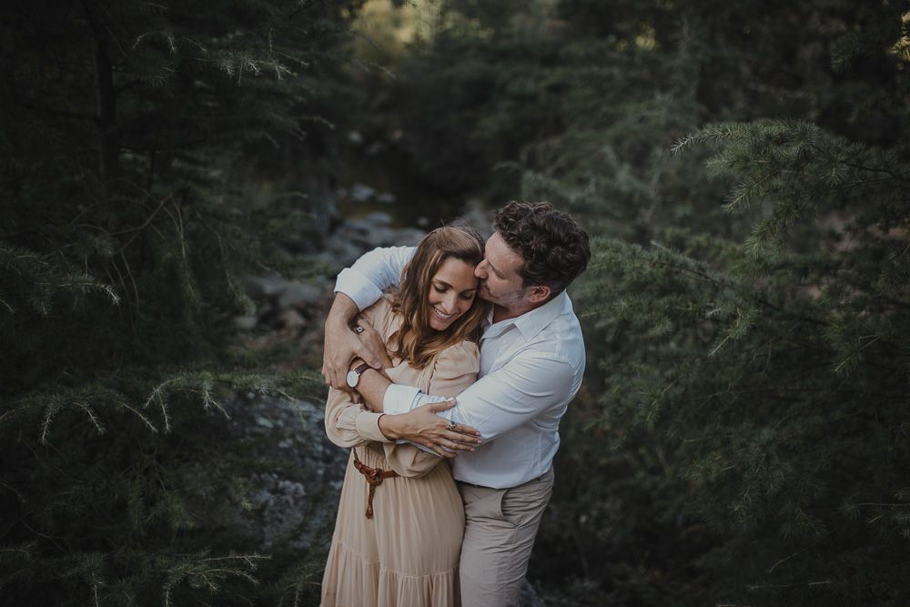 A loving couple shares an affectionate moment in a forest landscape.