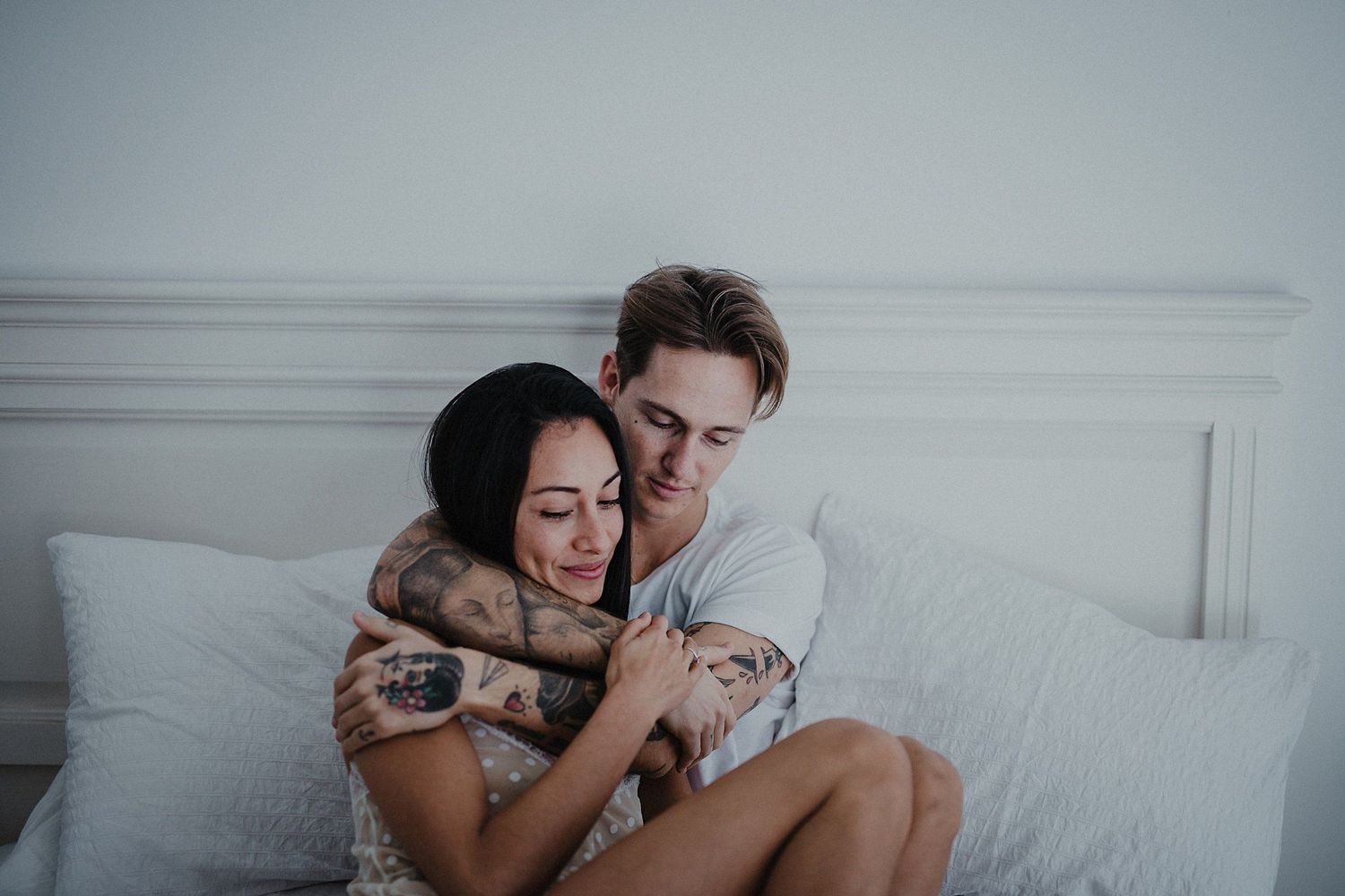 Couple sharing affectionate moments while cuddling on white bed.