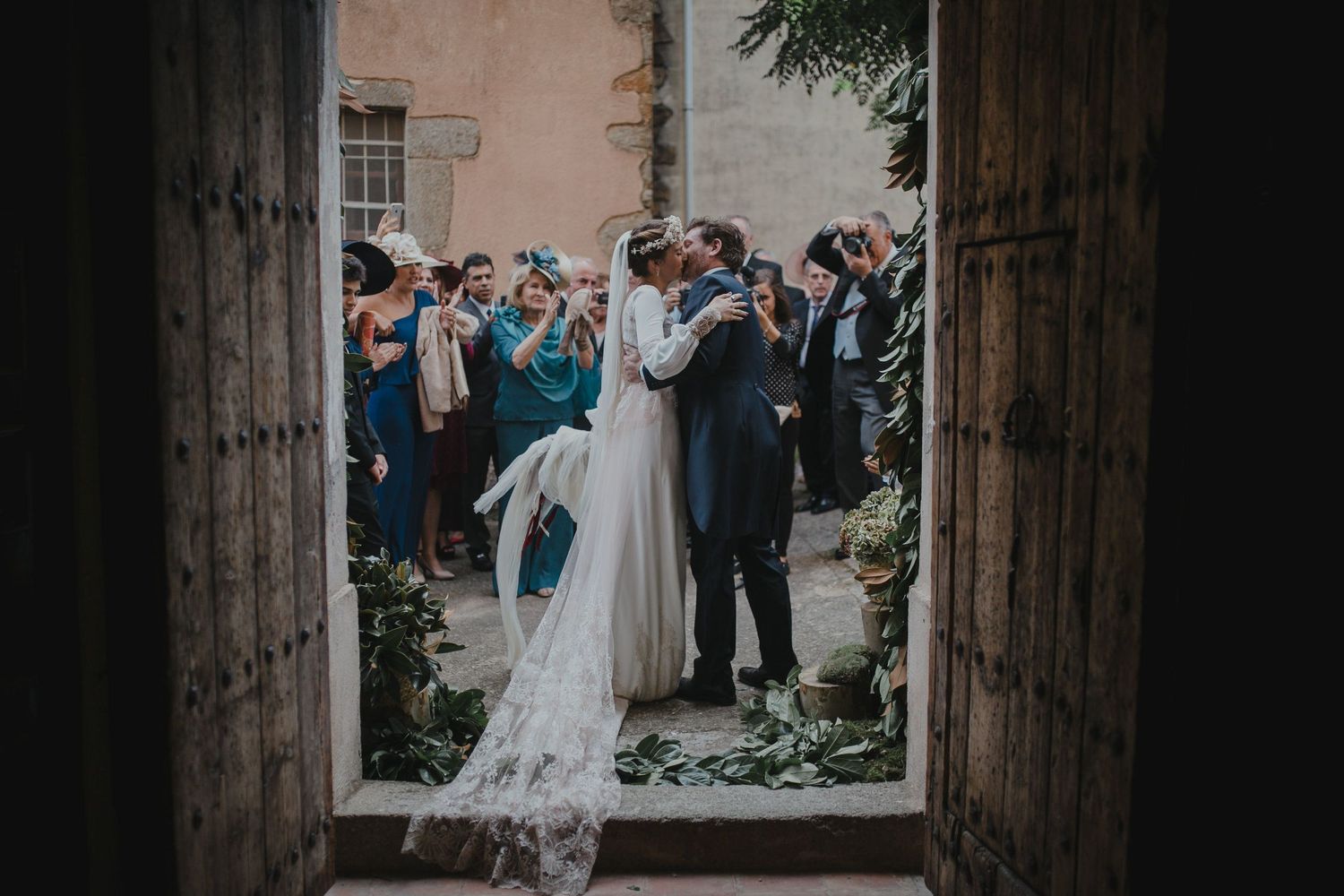 Newlyweds exit through historic wooden church doors as guests gather to celebrate on a sunny day.