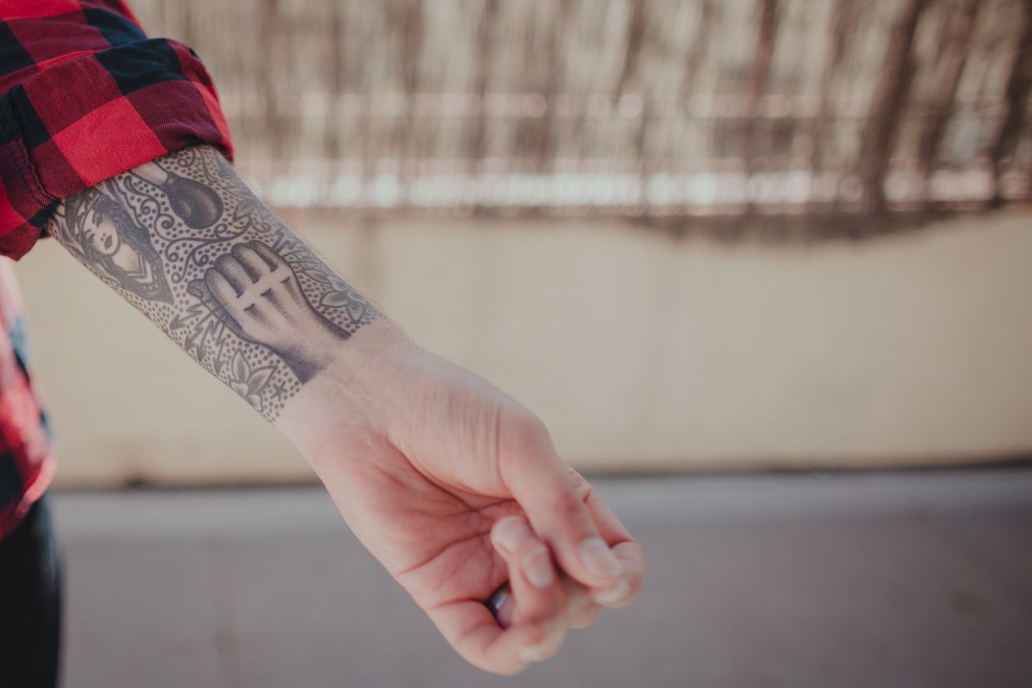 Close-up shot of a tattooed arm wearing a red plaid flannel sleeve.