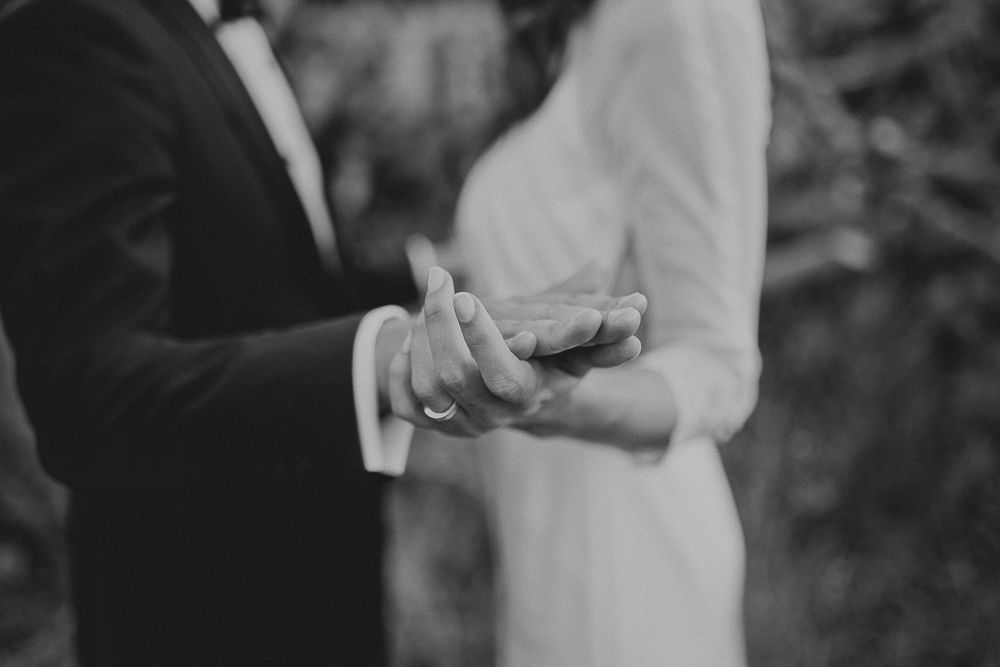 Black and white detail shot of couple's hands during ring exchange at wedding ceremony.