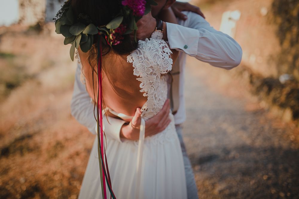 Close-up detail of wedding dress lace and floral bouquet with burgundy ribbons.