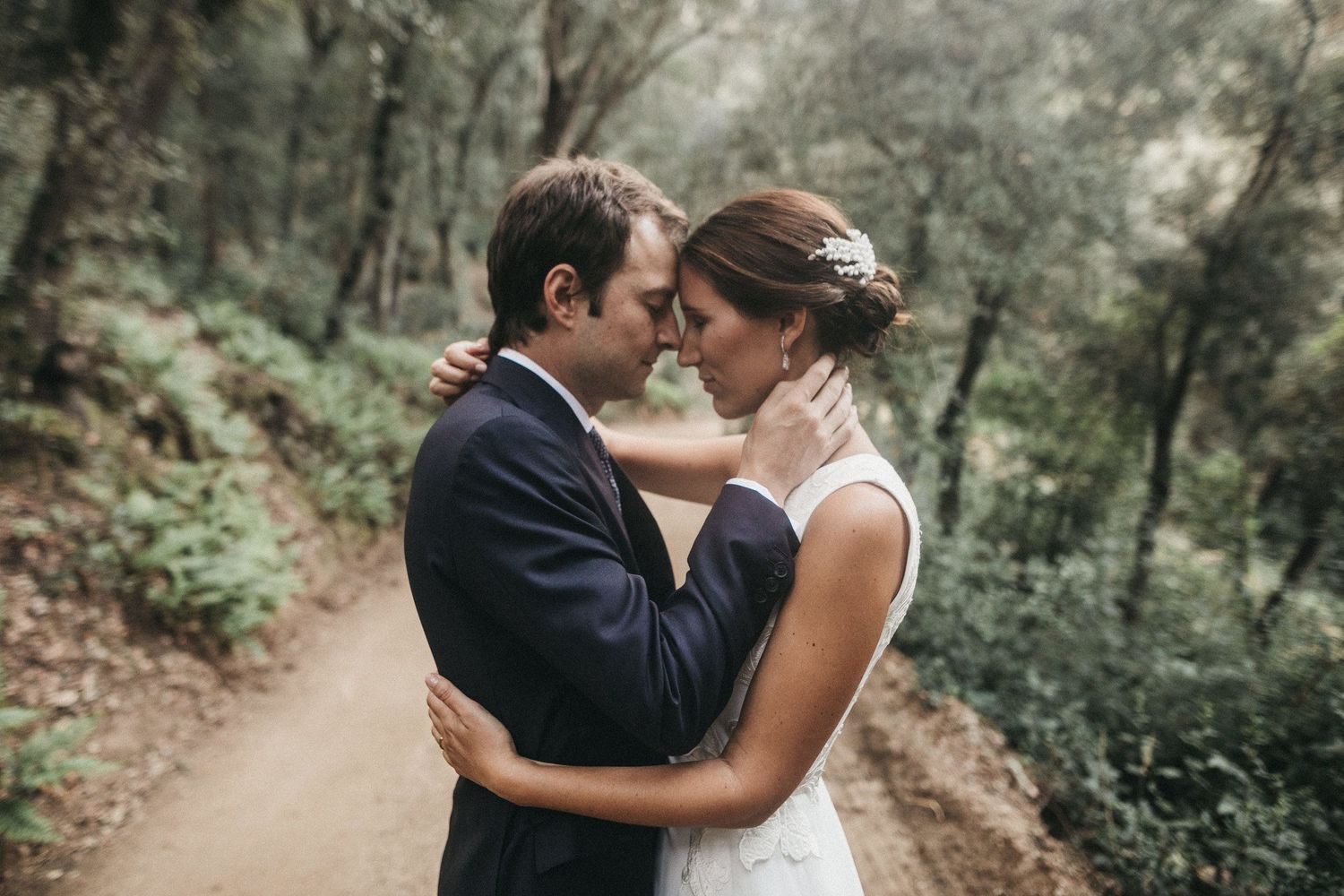 Intimate forest wedding portrait on dirt path surrounded by greenery.