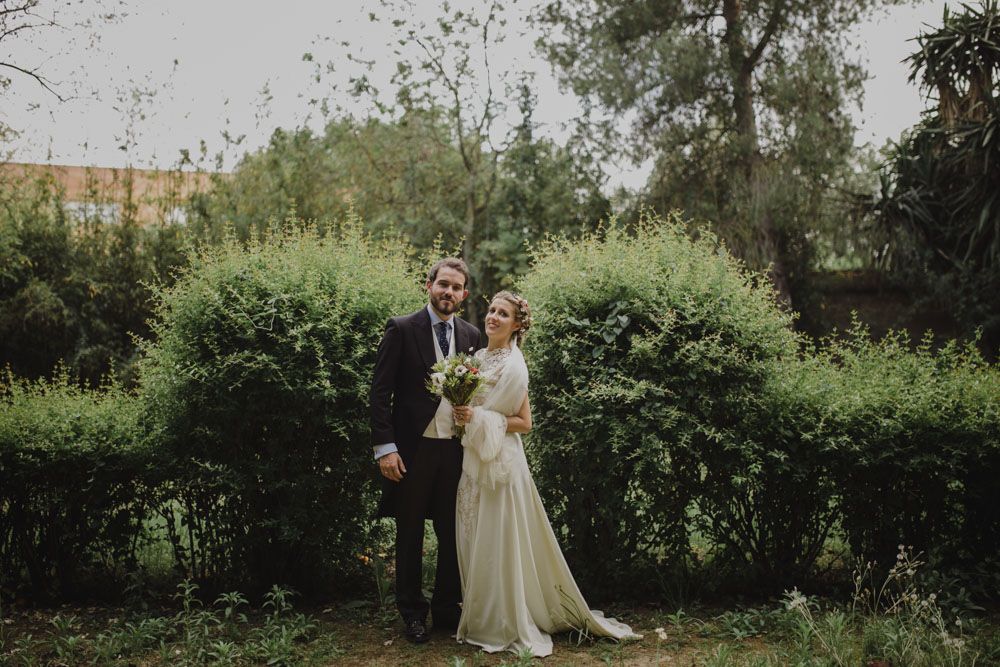 Classic wedding portrait of couple standing before hedge wall in garden setting.