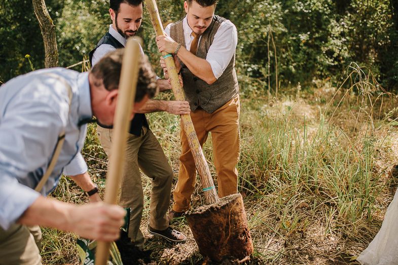 Groomsmen work together to dig a hole during outdoor wedding ceremony.
