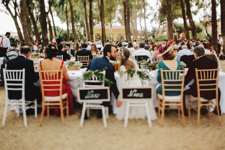 Outdoor wedding reception with colorful chairs and tables set among tall trees.