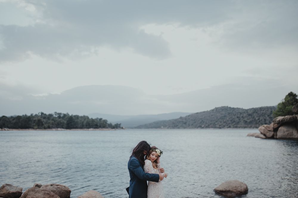 Intimate lakeside wedding moment with rocky shore and mountain vista.