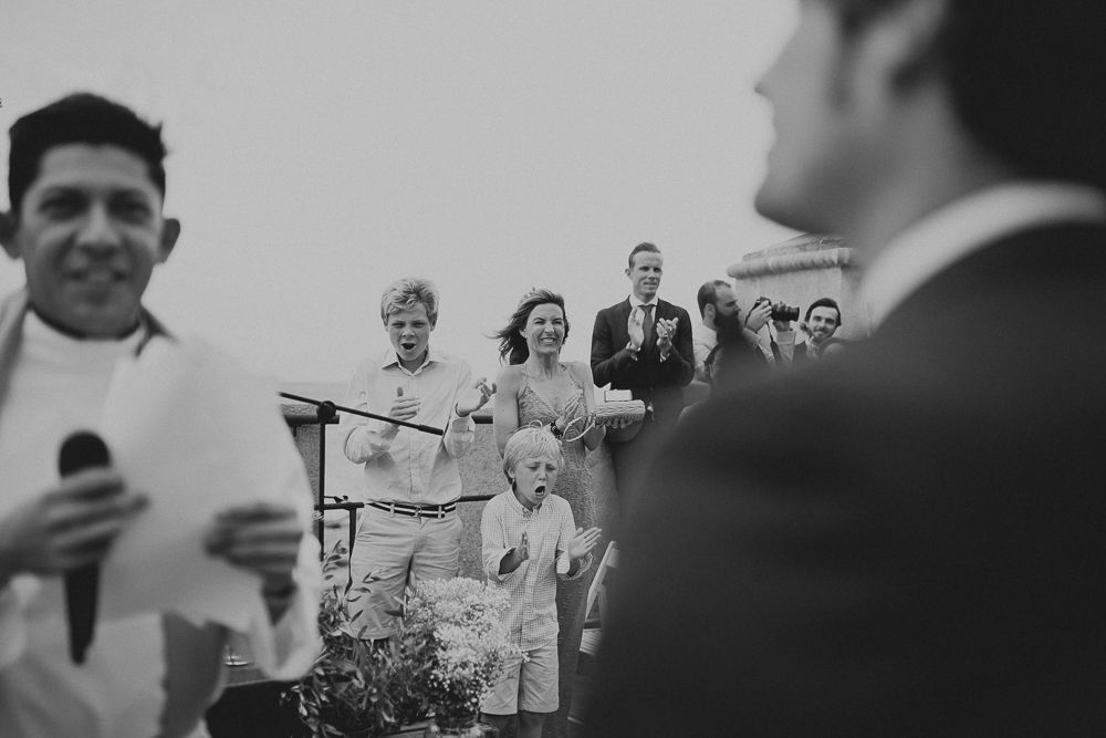Black and white photo of guests watching a wedding ceremony outdoors.