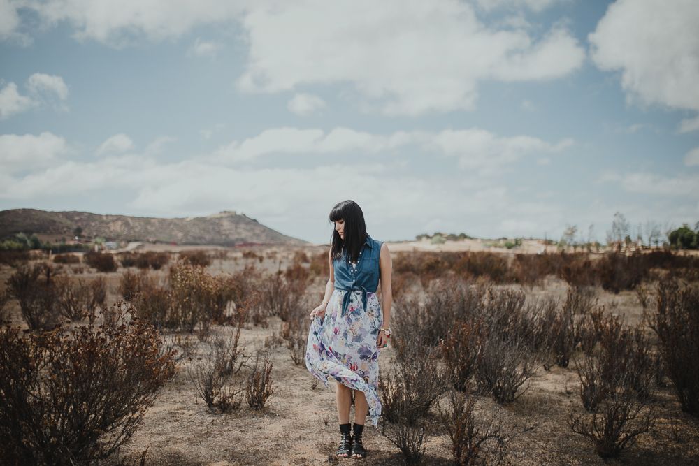 A floral dress contrasts against the desert brush and mountains on a bright sunny day.