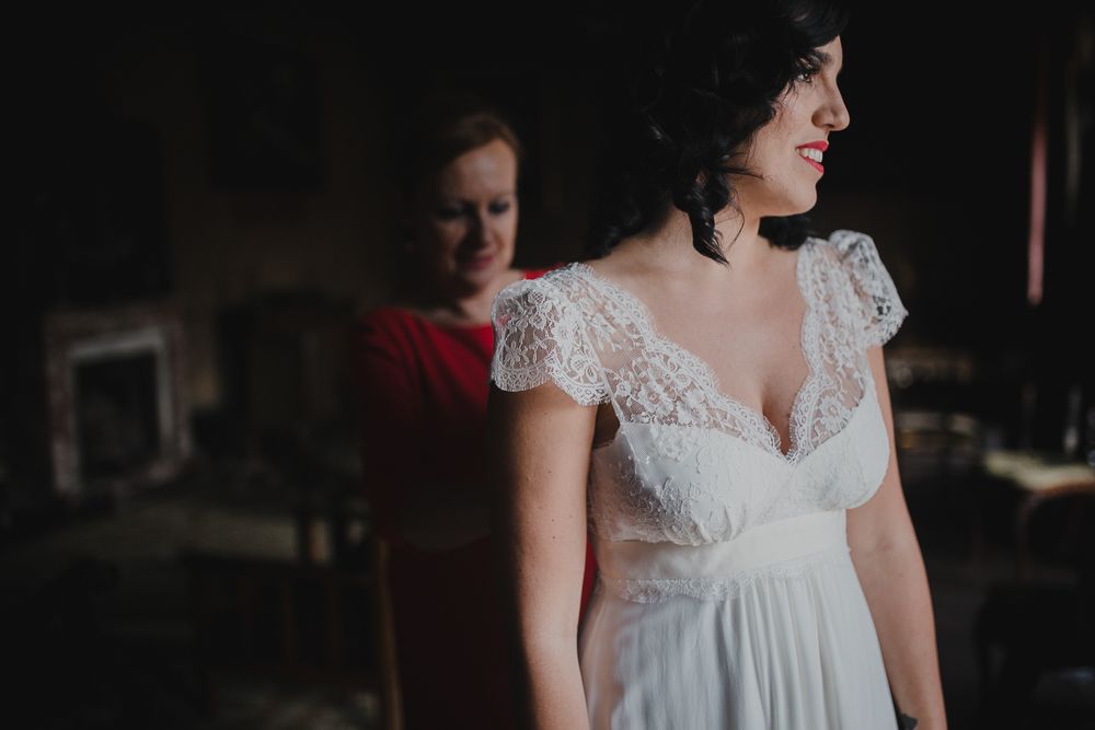 White lace wedding dress detail being adjusted in moody lighting.