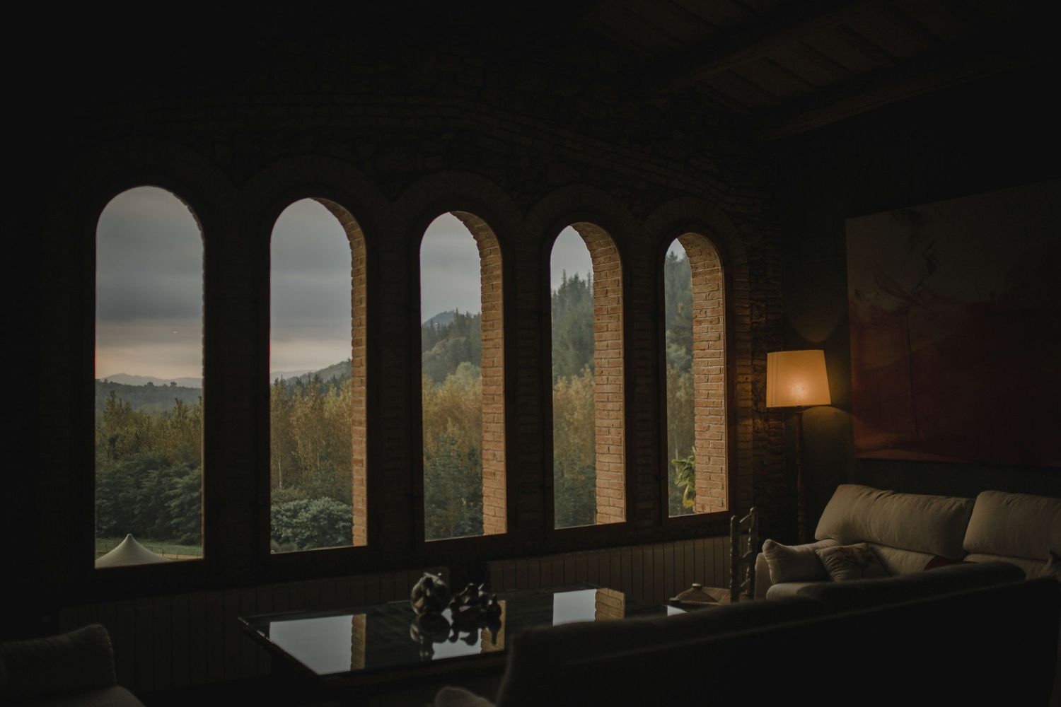 Arched windows frame scenic mountain views in dimly lit room with lamp.