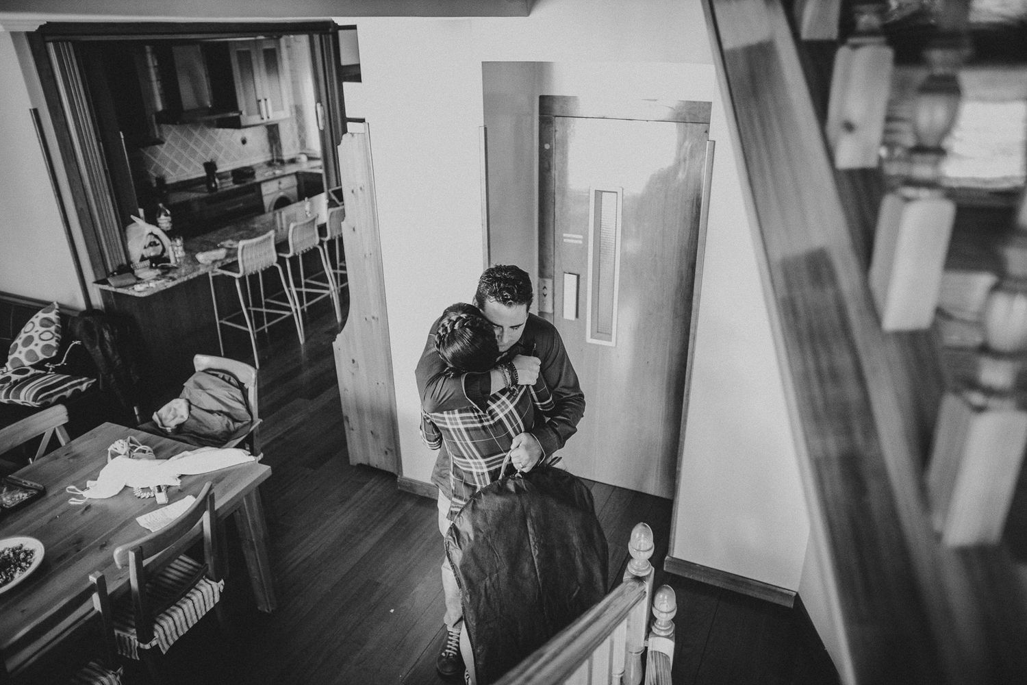 Black and white photograph of two people embracing in a home interior.
