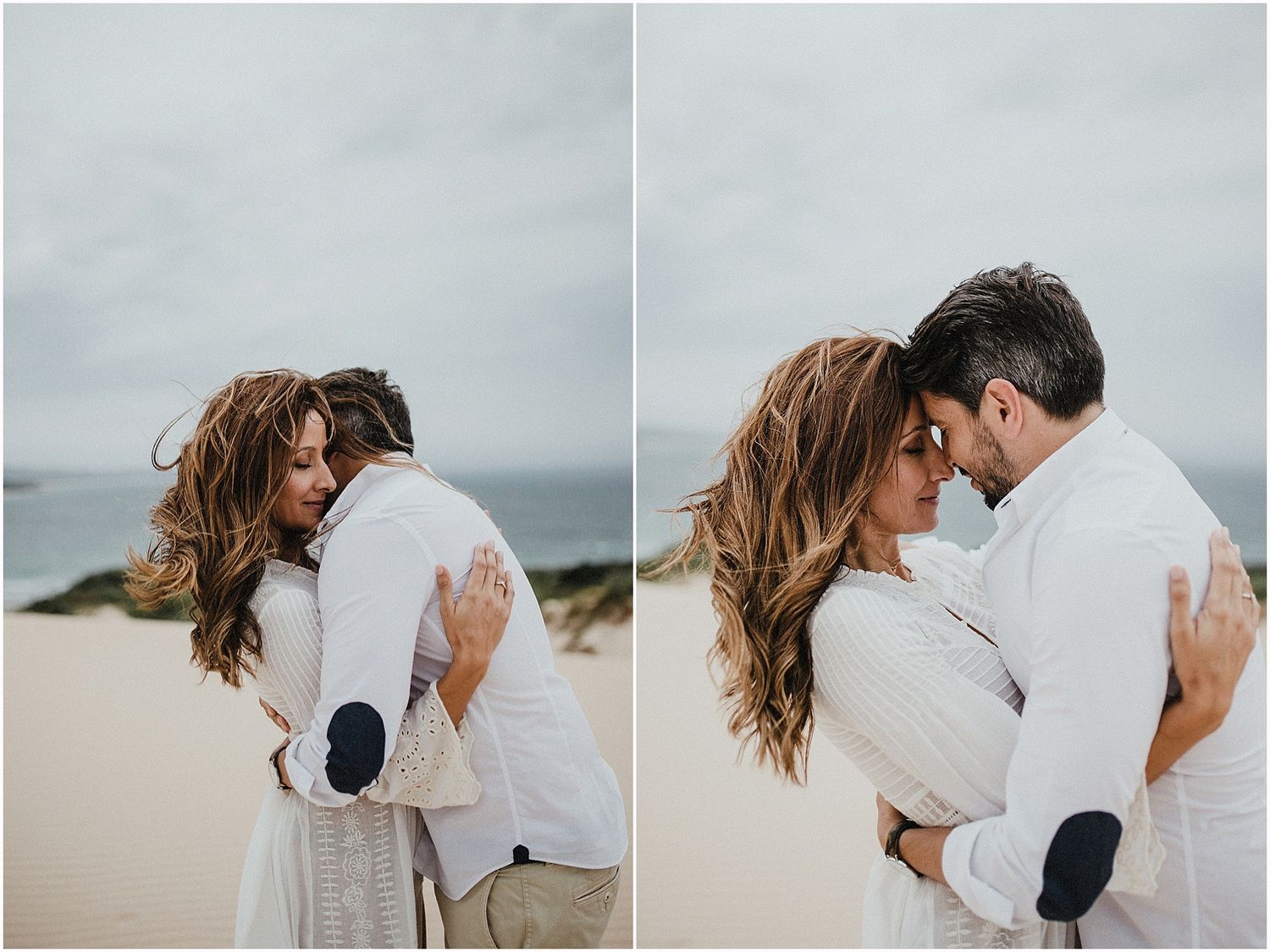 Intimate beach photoshoot showing a couple in white clothing embracing against cloudy coastal backdrop.
