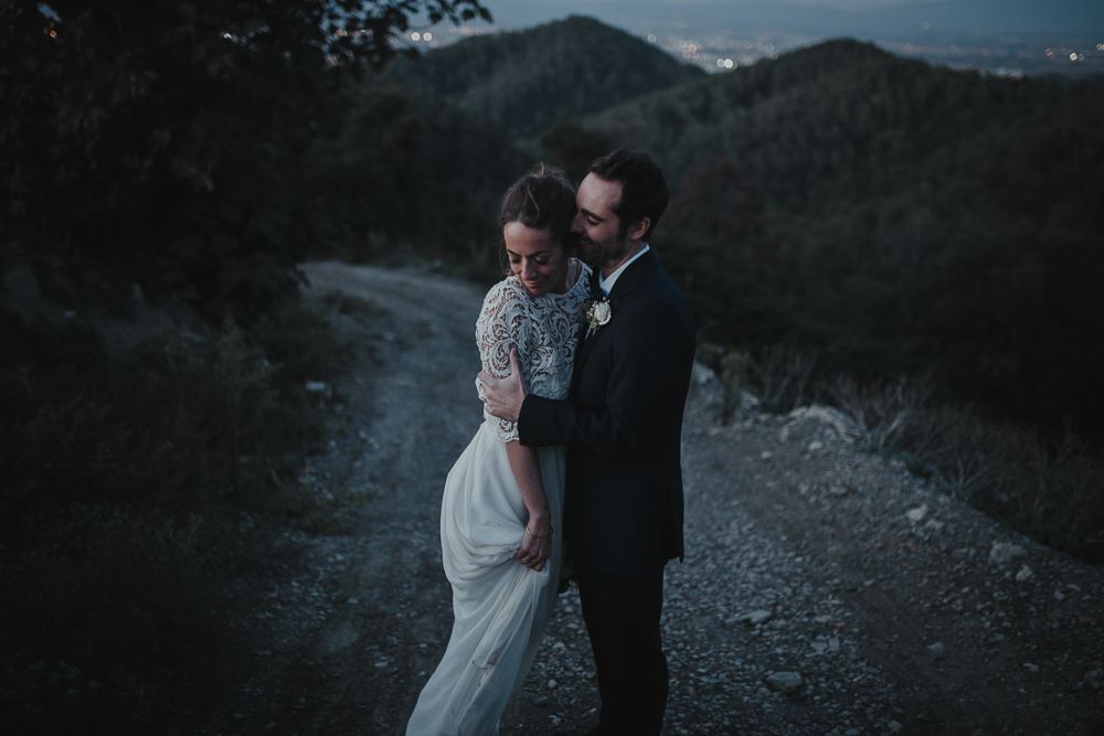 Couple shares tender moment on mountain path with scenic valley backdrop at dusk.