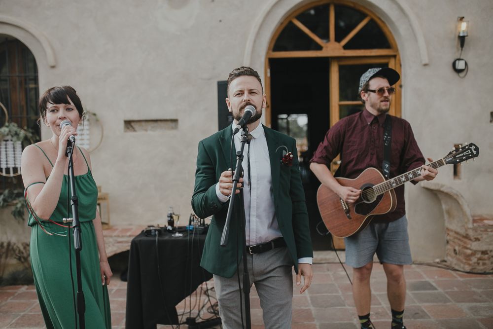 Live band performs at outdoor wedding venue with acoustic guitar and microphones.