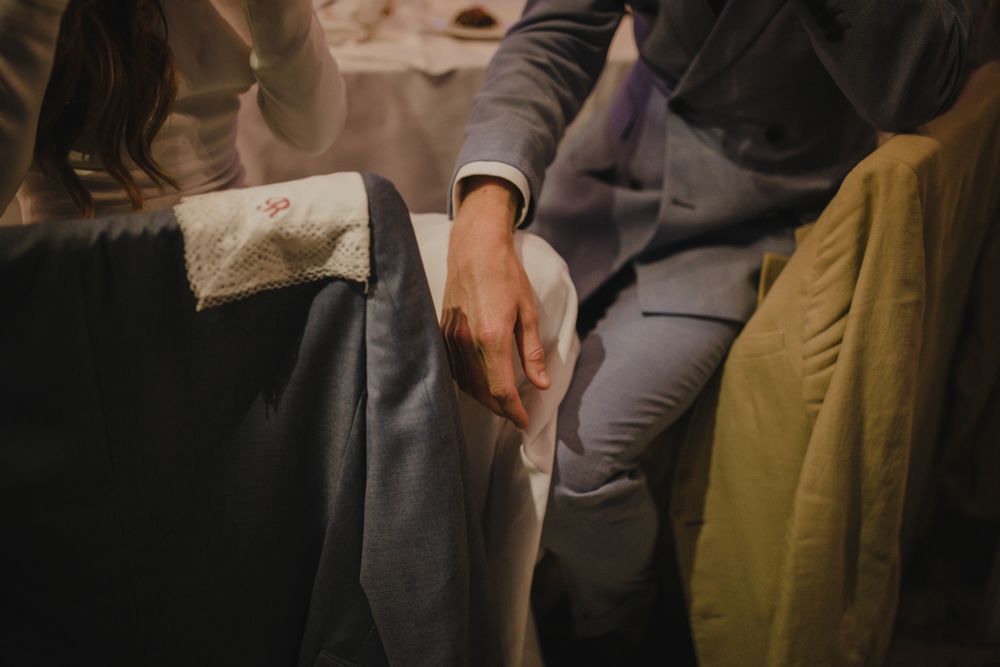 Close-up of formal attire and hands resting on grey upholstered seating.