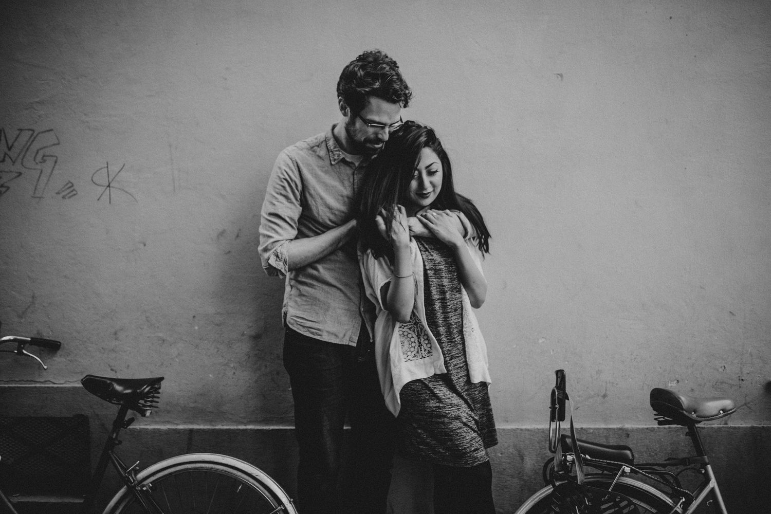 Intimate black and white portrait of couple leaning against wall next to vintage bicycle.