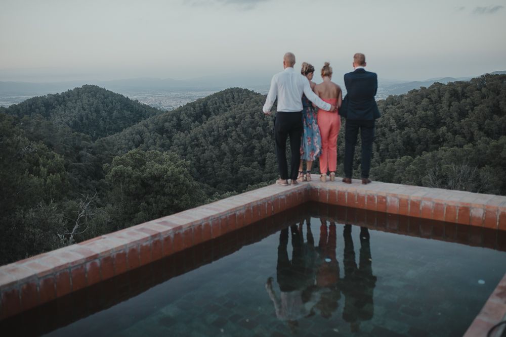 Three people stand at the edge of an infinity pool overlooking misty mountain views at sunset.