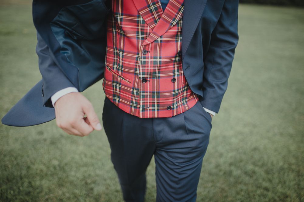 Detail shot of navy suit with red plaid waistcoat on grassy background.