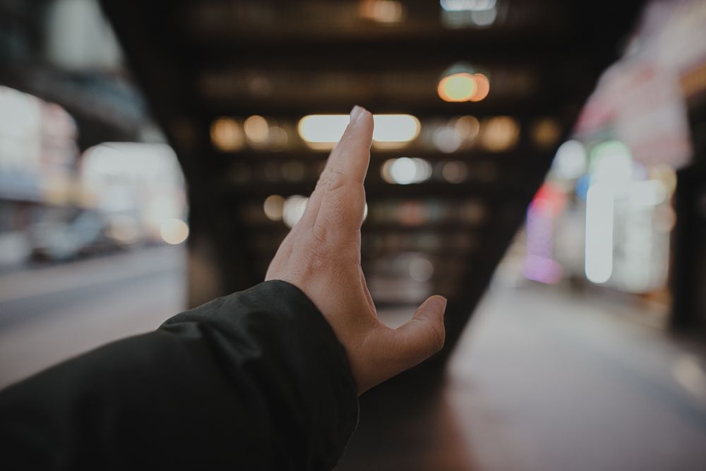 Hand reaching out against blurred urban background under elevated train tracks.
