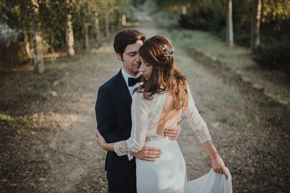Back view of newlyweds holding hands while walking through an orchard.