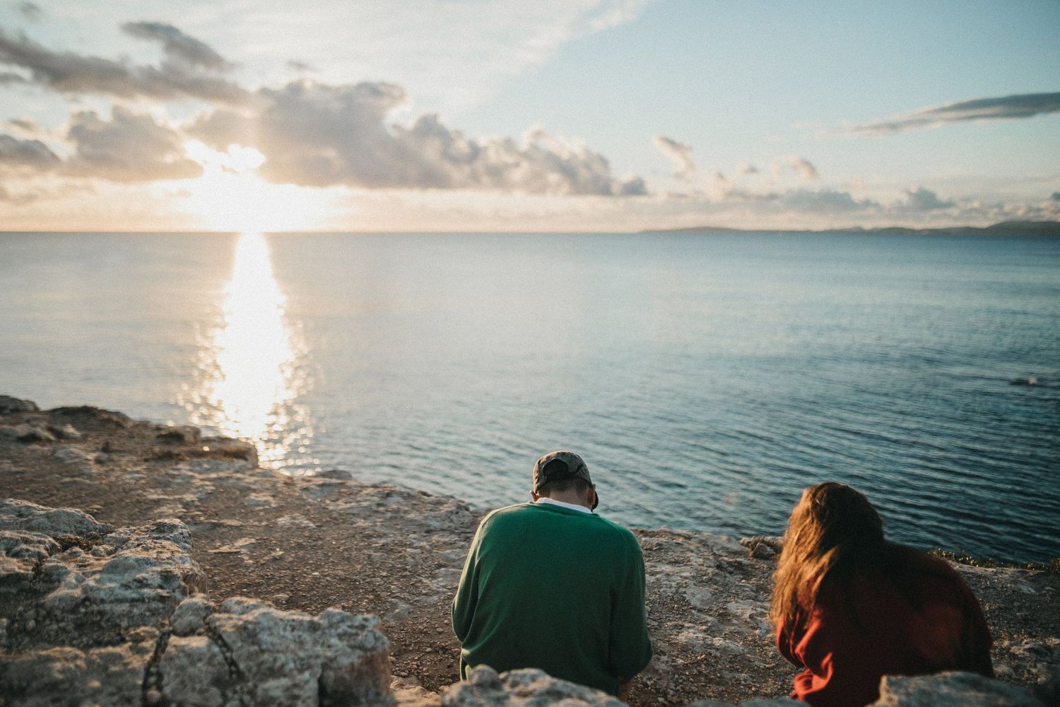 Two people sitting on coastal rocks watching a beautiful ocean sunset.