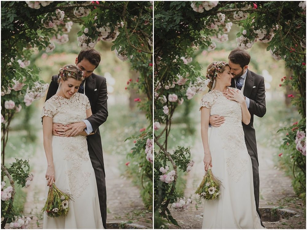 A tender wedding moment captured under blossoming trees in a garden setting.