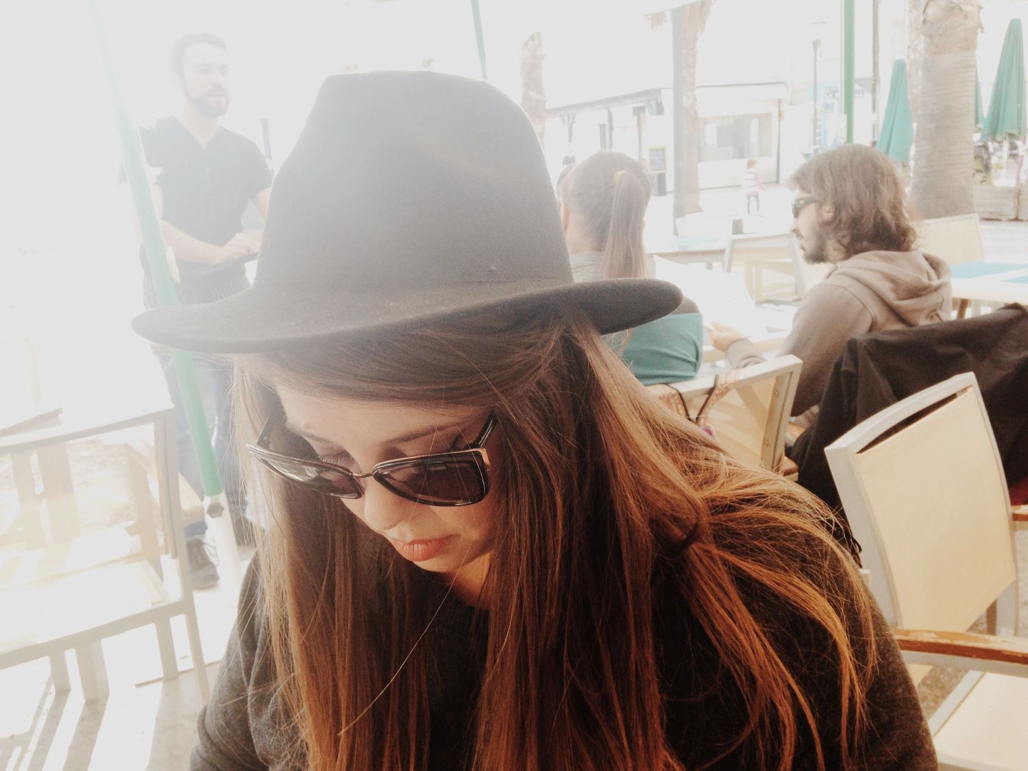 Person wearing a brown hat and sunglasses looking down with soft lighting.