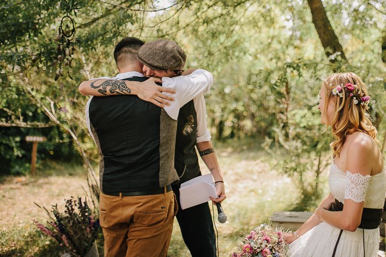 Emotional outdoor wedding ceremony moment between couple and officiant surrounded by trees.