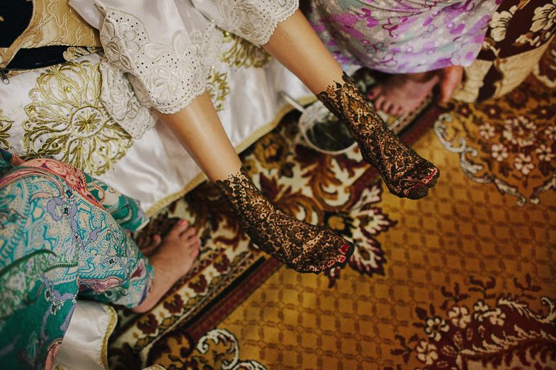 Close-up detail of traditional henna designs on hands with ornate fabrics and patterns.