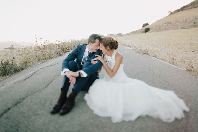 Couple in wedding attire sharing an intimate moment while sitting on a rural mountain road.