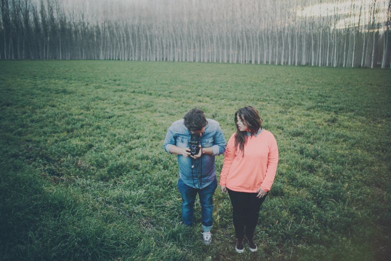 Two people standing in misty green field with row of tall trees in background.