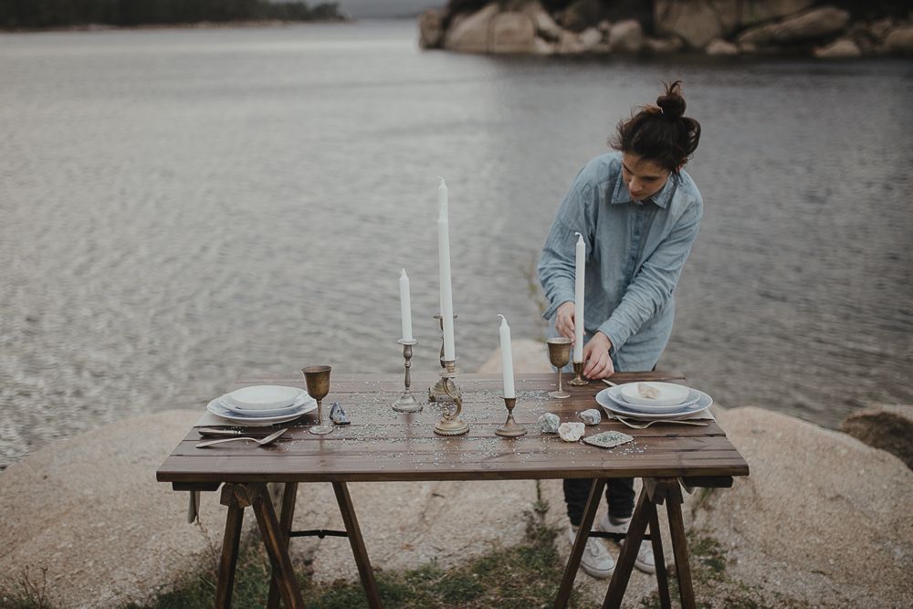 Romantic table setting being prepared on a wooden table by the lakeside.
