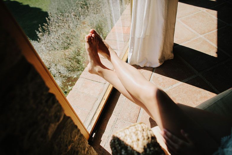 Sunlit feet resting on a window ledge with sheer curtains flowing in the breeze.