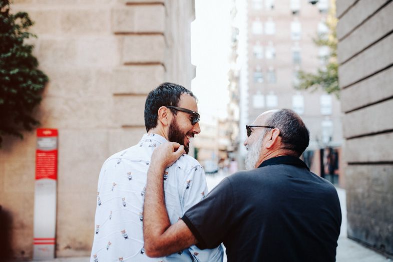 Two men having a conversation on a city street with buildings in the background.