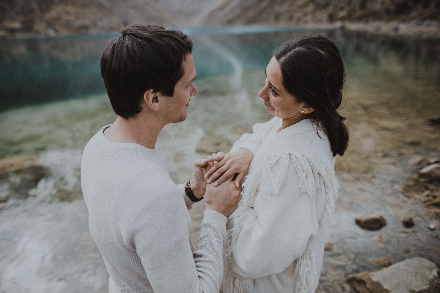 An intimate embrace photographed beside a scenic mountain lake with dramatic cliffs.