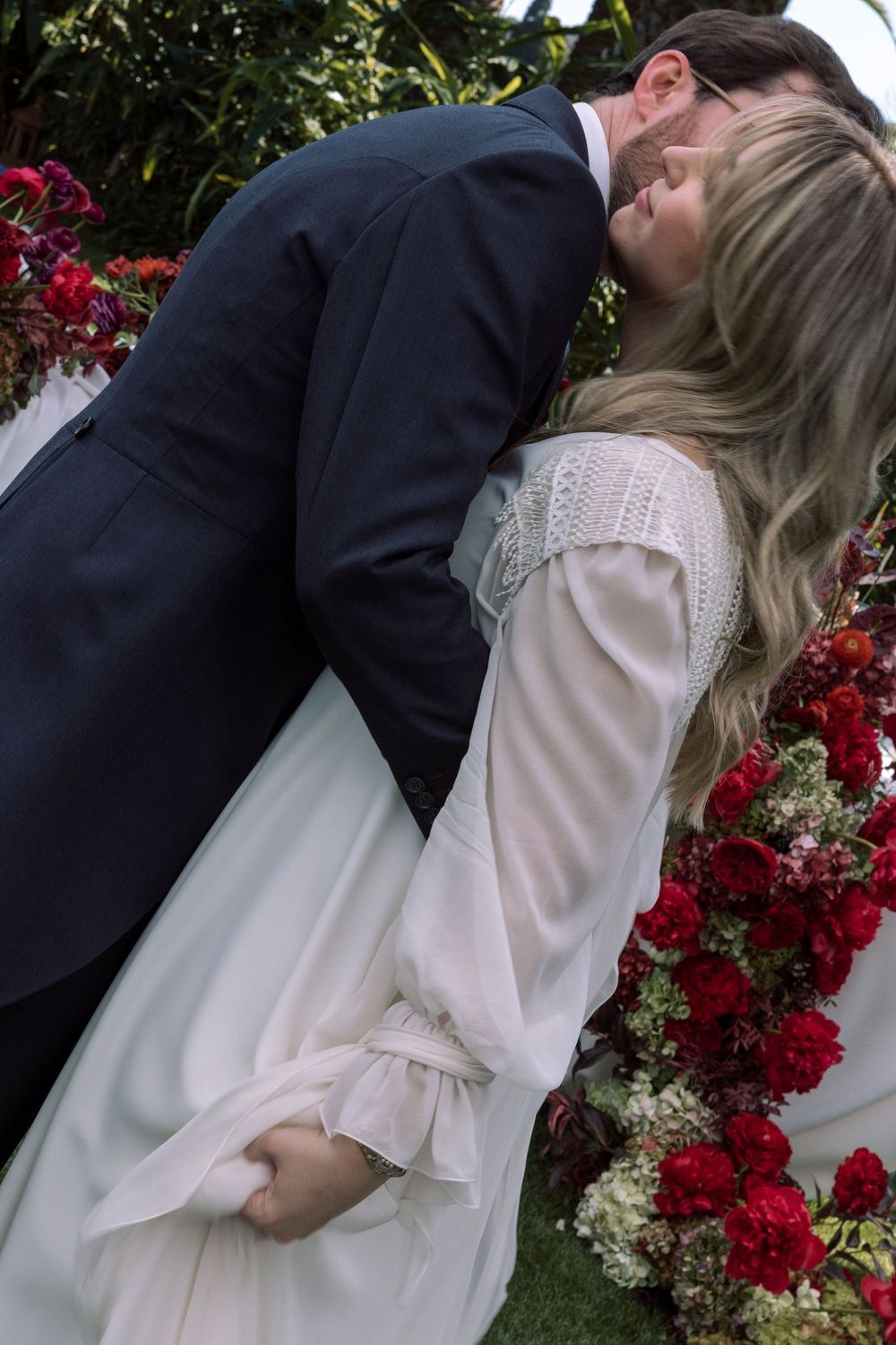 A romantic moment between newlyweds against a backdrop of red flowers.