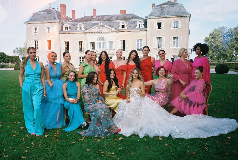 Wedding party in colorful dresses posing together on mansion grounds.