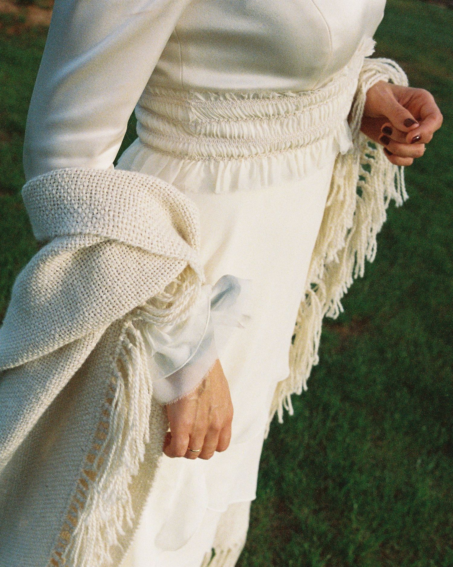 A close-up view of white knitted fringe details on a garment against a green grass background.