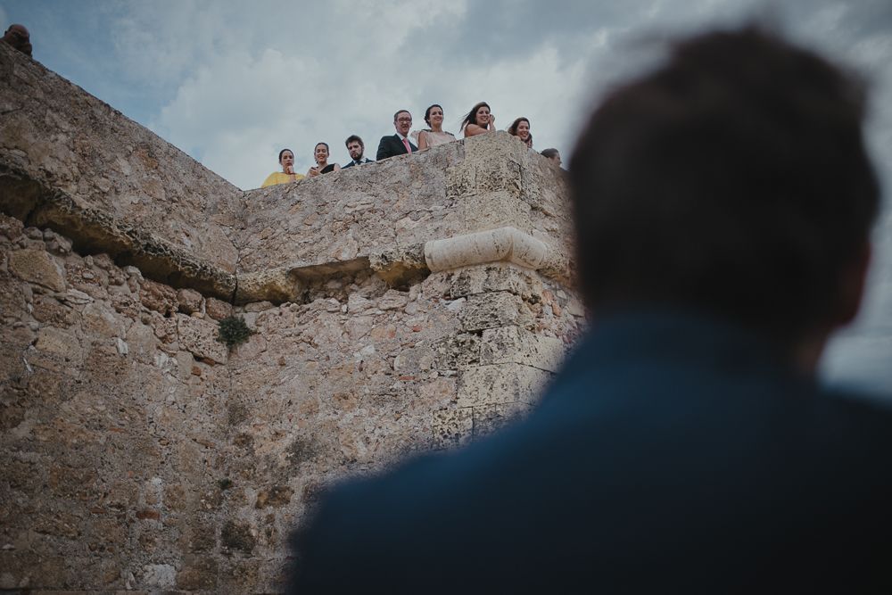 People gathered at the edge of an ancient stone wall looking down at someone below.