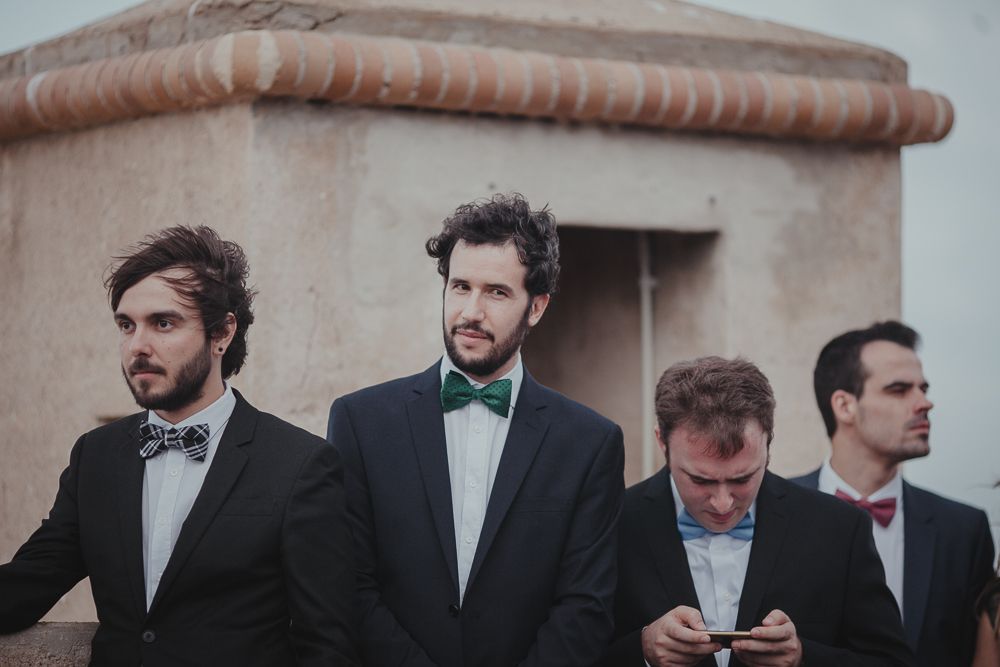 Groomsmen in formal suits and bowties stand together during a wedding ceremony.