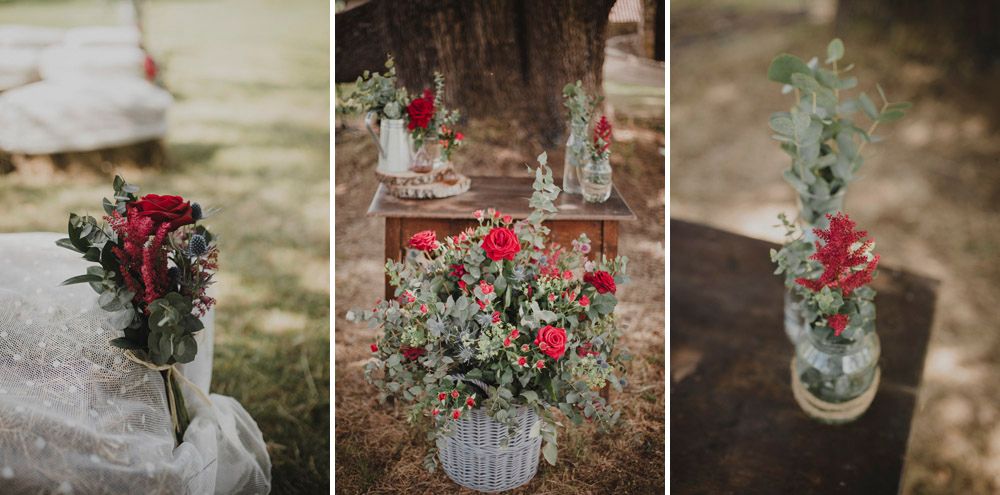 Red floral arrangements in vintage-style vases and jars as rustic wedding decorations.
